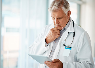 Image showing One mature male doctor thinking while browsing on a digital tablet device in a hospital or clinic. Senior caucasian man working with apps online to check medical records and research with telemedicin