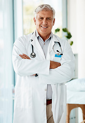 Image showing Experienced mature male doctor smiling and standing with his arms crossed in a hospital. One optimistic senior man wearing a lab coat looking confident and happy to give a patient good news