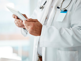 Image showing Closeup of expert male doctor holding and using a digital tablet, working at a hospital alone. One caucasian man wearing a labcoat working on a digital tablet standing in an office at a clinic