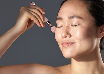 Image showing This is the most wonderful skincare tool I have ever used. Studio shot of a beautiful young woman using a face roller on her skin.