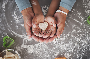 Image showing Cookies are made of butter and love. an unrecognizable girl and her mom holding a heart shaped cookie in the kitchen at home.