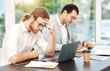 Image showing I just cant focus today. a young businessman looking stressed out while working on a laptop in an office with his colleague in the background.