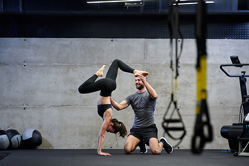 Image showing A muscular man assisting a fit woman in a modern gym as they engage in various body exercises and muscle stretches, showcasing their dedication to fitness and benefiting from teamwork and support