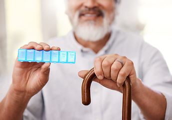 Image showing This helps me to remember what medication to take. a senior man sitting with a walking stick and holding up a weekly pill box.