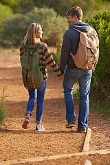 Image showing On the trail of love. Rear view shot of a young couple holding hands and walking down a hiking trail.