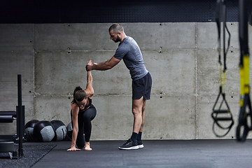 Image showing A muscular man assisting a fit woman in a modern gym as they engage in various body exercises and muscle stretches, showcasing their dedication to fitness and benefiting from teamwork and support