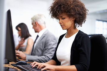 Image showing Working hard to get the job done. an attractive young working at a desk with her colleagues in the background.