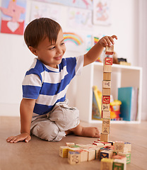 Image showing Make the tower bigger. A young boy playing with his building blocks in his room.
