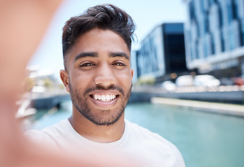 Image showing Young mixed race sportsman smiling and holding mobile phone with hand to take a selfie while out for a run or jog along a water canal in the city. Happy male athlete taking self-portrait during worko