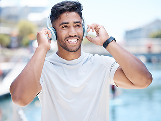 Image showing Happy young mixed race male athlete smiling while putting on his headphones before a run or jog and looking away outdoors. Fit sportsman listening to music while exercising