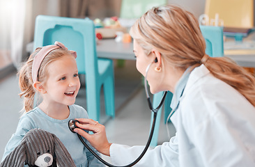 Image showing Young caucasian female doctor doing a checkup on a happy and cheerful little at a hospital. Carefree little girl smiling while holding a toy during a medical exam at daycare.