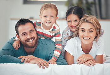 Image showing Happy caucasian family of four in pyjamas cosy together in bed at home. Two little kids lying on top of their loving parents. Adorable playful young girls bonding with their mom and dad during bedtim