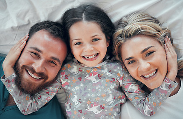 Image showing Happy carefree caucasian family in pyjamas from above lying cosy together in bed at home. Loving parents with their little daughter. Adorable young girl hugging her mom and dads face during bedtime