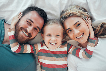 Image showing Happy smiling caucasian family of three looking cosy together in bed at home. Loving parents with their little daughter. Adorable young girl hugging her mom and dads face and taking a selfie