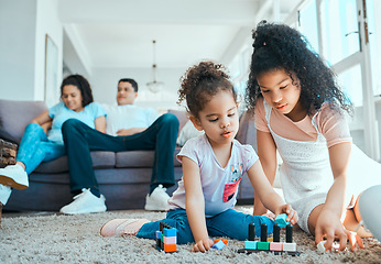 Image showing We prefer building new toys. two sister playing on the floor while their parents relax in the background.