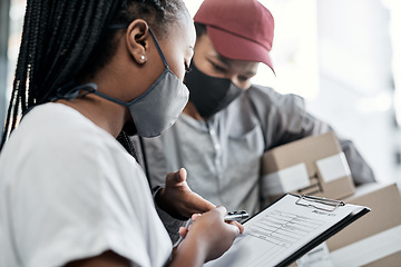 Image showing Nothing satisfies a customer like same day delivery. a masked young woman signing for a delivery received at home.