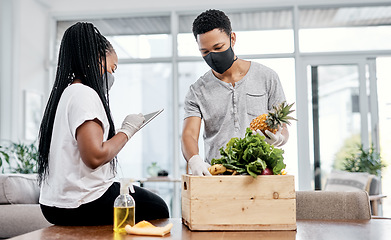 Image showing Making sure their order is in order. a masked young couple using a digital tablet while disinfecting their groceries at home.
