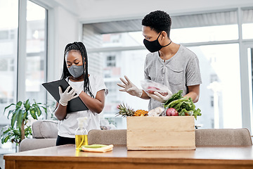 Image showing When unpacking groceries turns into a production line. a masked young couple disinfecting their groceries at home.