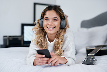 Image showing Music always make me feel good. a young woman wearing headphones and holding her cellphone while lying on her bed.