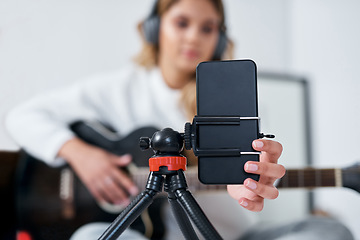 Image showing I use my music to express myself. a young woman using her cellphone to record herself while playing the guitar at home.