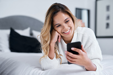 Image showing Theres so many fun things to keep you busy online. a young woman using her cellphone while lying on her bed.