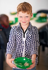 Image showing I finished it all. Portrait of a little boy with a plate of food with volunteers serving food in the background.