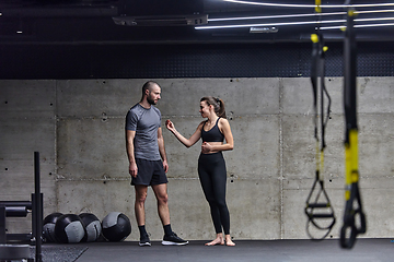 Image showing Muscular man and fit woman in a conversation before commencing their training session in a modern gym.
