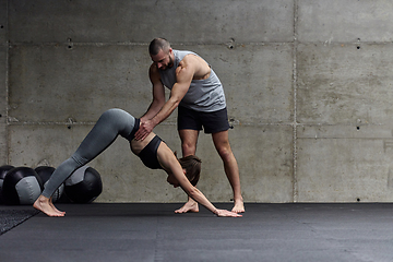 Image showing A muscular man assisting a fit woman in a modern gym as they engage in various body exercises and muscle stretches, showcasing their dedication to fitness and benefiting from teamwork and support