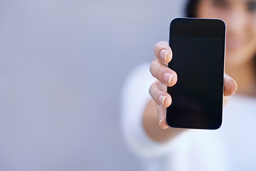 Image showing You have to get this phone. Portrait of a young woman standing against a grey background and holding up her mobile phone.