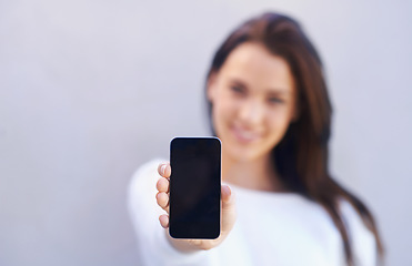 Image showing This is the best phone on the market. Portrait of an attractive young woman standing against a gray background and holding up her mobile phone.