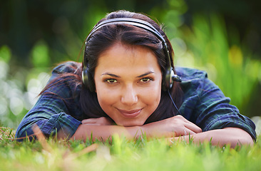 Image showing You never know what you might find in the long grass. Portrait of an attractive young woman lying on the grass and listening to music.