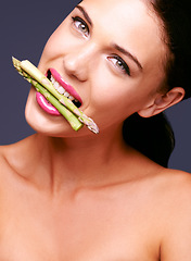 Image showing How could you say no to veggies now. Portrait of a woman biting on a bunch of asparagus in studio.