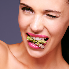 Image showing Vegetables have never been sexier. Portrait of a beautiful woman winking while biting on a bunch of asparagus in studio.