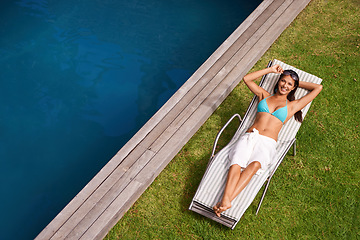 Image showing Sunshine and happiness. Portrait of a beautiful young woman relaxing in a lounge chair by a swimming pool.