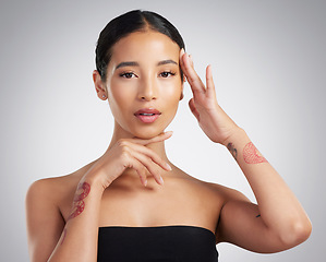 Image showing Portrait of a beautiful mixed race woman touching smooth soft skin in a studio. Hispanic model with healthy natural glowing skin looking confident against grey copyspace while doing routine skincare