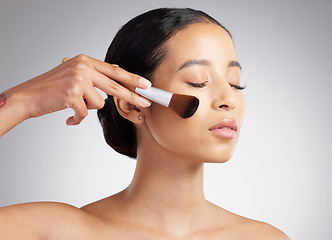 Image showing A beautiful mixed race woman posing with a makeup brush during a pamper routine. Hispanic model holding a contouring brush against a grey copyspace background