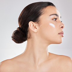Image showing A little goes a long way. a young woman applying a cream to her face against a grey background.