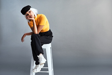 Image showing A timeless hat with an updated look. Studio shot of a beautiful young woman sitting on a stool against a grey background.