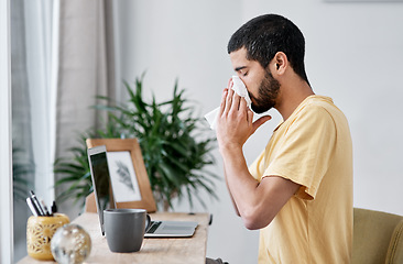 Image showing Until he gets better, home is his place of business. a young man blowing his nose while working from home.