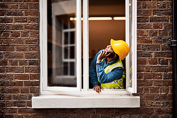 Image showing I see the problem. a young engineer talking on his cellphone while looking out the window of a construction site.