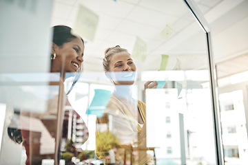 Image showing Laying out a timeline of anticipated profits. two businesswomen brainstorming with notes on a glass wall in an office.