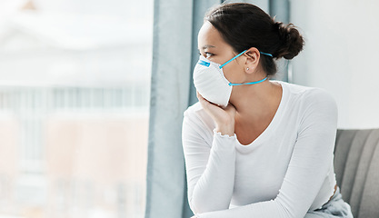 Image showing The best way to protect yourself is to stay in. a young woman wearing a mask while looking out a window at home.