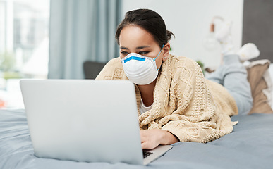 Image showing Checking for updates and the latest news on the virus. a woman wearing a mask while lying on her bed with her laptop.