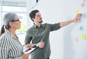 Image showing Running through their master plan. two businesspeople brainstorming with notes on a wall in an office.