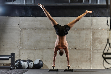 Image showing A muscular man in a handstand position, showcasing his exceptional balance and body control while performing a variety of exercises to enhance his overall body stability and strength in a modern gym