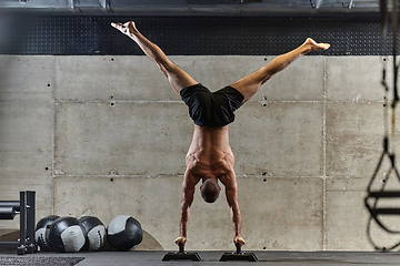 Image showing A muscular man in a handstand position, showcasing his exceptional balance and body control while performing a variety of exercises to enhance his overall body stability and strength in a modern gym