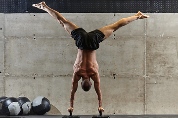 Image showing A muscular man in a handstand position, showcasing his exceptional balance and body control while performing a variety of exercises to enhance his overall body stability and strength in a modern gym