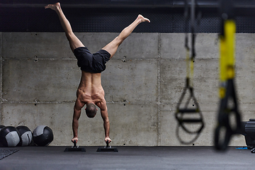 Image showing A muscular man in a handstand position, showcasing his exceptional balance and body control while performing a variety of exercises to enhance his overall body stability and strength in a modern gym