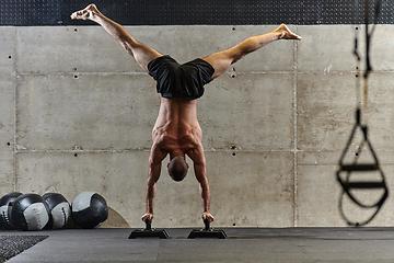 Image showing A muscular man in a handstand position, showcasing his exceptional balance and body control while performing a variety of exercises to enhance his overall body stability and strength in a modern gym