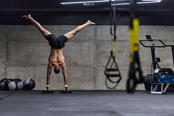 Image showing A muscular man in a handstand position, showcasing his exceptional balance and body control while performing a variety of exercises to enhance his overall body stability and strength in a modern gym